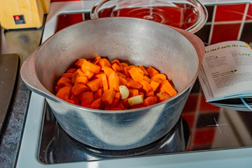  Chopped carrots and garlic cloves in a stainless-steel saucepan on the hob when making healthy and nutritious homemade soup