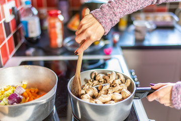 Home chef cooking mushrooms in a stainless-steel saucepan on the hob - just one stage of making a healthy and nutritious mushroom and pasta dinner