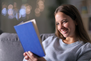  Happy woman reading a paper book on a couch in the night