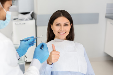 Satisfied young lady in dentist chair showing thumb up