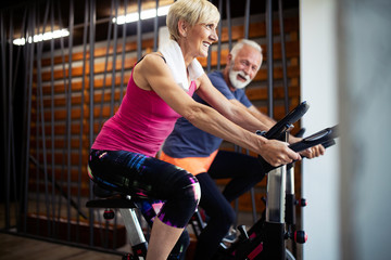 Happy fit mature woman and man cycling on exercise bikes to stay healthy