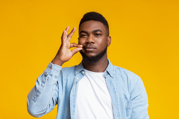 Attractive black man zipping his mouth shut on yellow background