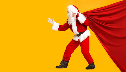 Fototapeta na wymiar Santa trying to pull big bag with Christmas gifts on orange