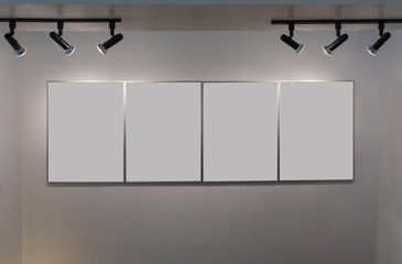 Four modern picture frames on the gray wall with lamp lighting with blank space for text and...
