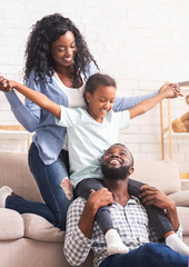 Black parents and little daughter having fun at home together.