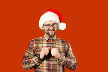 Handsome bearded man in Santa hat and glasses. Santa man pointing to the side over white wall. Christmas concept. Mock up, copy space for text. Hipster bearded man thinking for christmas gift ideas