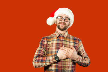 Handsome bearded man in Santa hat and glasses. Santa man pointing to the side over white wall. Christmas concept. Mock up, copy space for text. Hipster bearded man thinking for christmas gift ideas