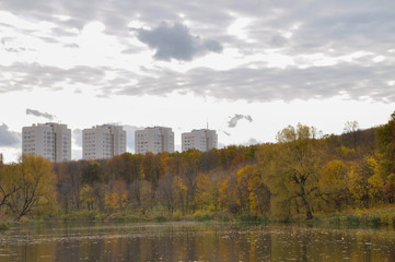 Landscape in cloudy october day with pond, trees and buildings