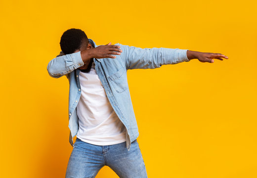 Black guy throwing dab move over yellow background in studio