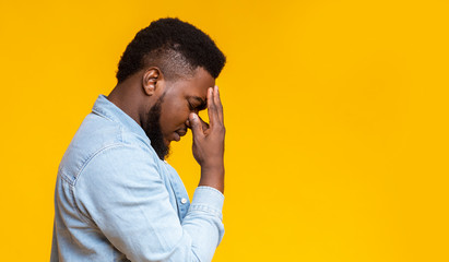 Profile portrait of depressed black guy touching his forehead