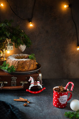 Chrismas festive atmosphere. Cake with dried fruits decorated with sugar powder and spruce branches with garland on the background. Copy space. Side view. Bakery, christmas pastry