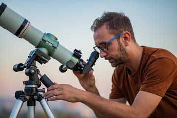 Astronomer with a telescope watching at the stars and Moon with blurred city background.
