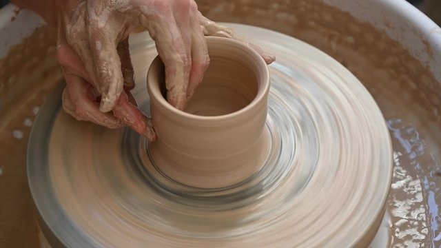 Hands of potter creating a jar on circle