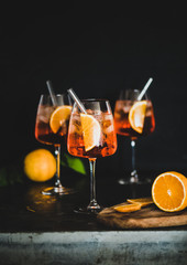 Aperol Spritz aperitif with oranges and ice in glass with eco-friendly glass straw on concrete table, black background, selective focus, copy space. Summer refreshing drink concept - obrazy, fototapety, plakaty