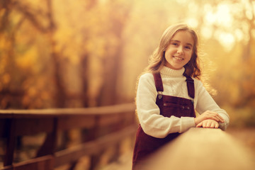 cheerful preteen girl looking at the camera standing on the bridge in the park, copy space