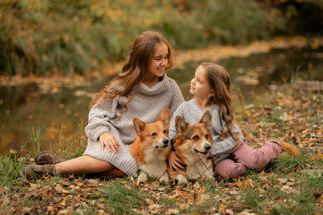 two sisters sitting on the ground with dogs in the autumn park