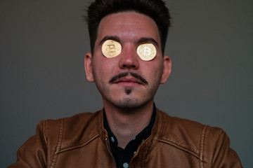 young man with bitcoins in the eye sockets on a dark background. portrait. close-up. emotions
