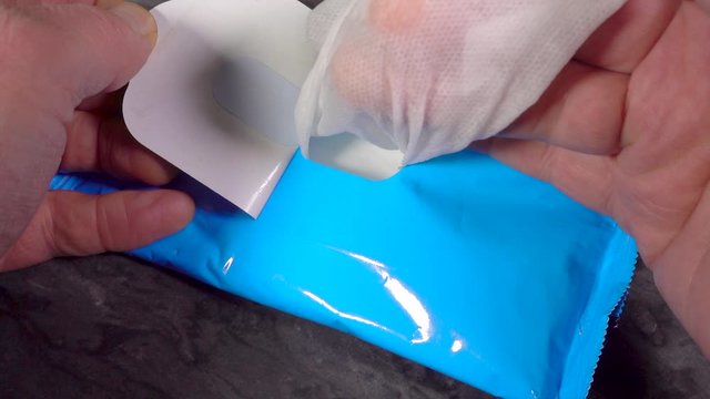 Slow motion close POV shot of a man&rsquo;s hand holding the flap of a blue re-sealable pack, while pulling out an antispectic wet wipe, to disinfect hands.