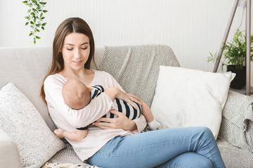 Mom holding newborn child, lulling baby on couh at home