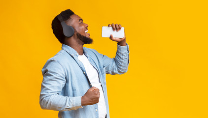 Cheerful african american man singing into smartphone like microphone