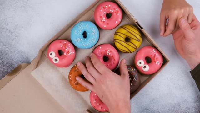 Top view of delicious sweet donuts. Loving couple at a meeting on Valentine's Day take donuts out of the box on a grey table background, slow motion.