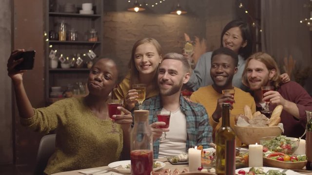 Handheld shot of happy people smiling and taking selfie at dinner party in cozy home