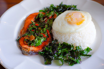 Grilled salmon stir-fried with spicy Thai basil and hot chilli with rice topping with fried egg. Thai food spicy dish top view.