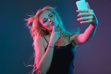 Caucasian young woman's portrait on gradient background in neon light. Beautiful female model with unusual look. Concept of human emotions, facial expression, sales, ad. Making selfie, bet, purchases.