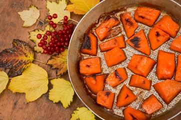  Fried baked on grill pumpkin, a traditional autumn snack.Warm dish as a dessert.On a baking sheet, on a rustic wooden old table with yellow leaves and viburnum.Top view copy space,food for Halloween