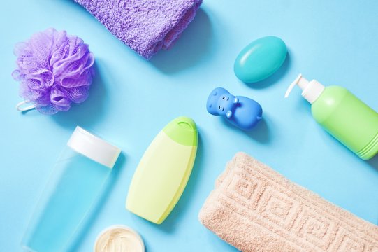 Purple sponge, moisturizing organic shower gel, green shampoo bottle, liquid soap and bar, rolled cotton towels and body cream on a light blue background. Flat lay photo baby care cosmetic products