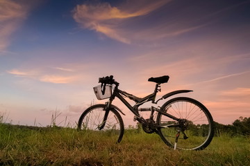 Fototapeta na wymiar Mountain view even Silhouette a bicycle parking on grass field around with forest, mountain and cloudy sky background, sunset at Thung Salang Luang National Park, Phetchabun, Thailand.