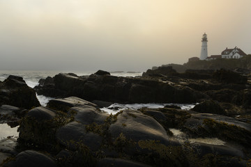 Fototapeta na wymiar The dramatic landscape of the rocky shore and the lighthouse on the shore in the fog. USA. Maine Portland