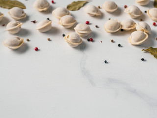 Fototapeta na wymiar Pattern of frozen uncooked russian pelmeni with peppercorns and bay leaves on white marble table. Creative layout of dumplings. Beautiful scattered raw dumplings. Top view or flat lay. Copy space