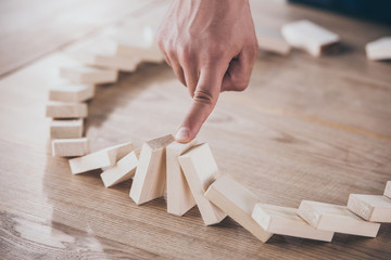 cropped view of businessman stopping domino effect of falling wooden blocks