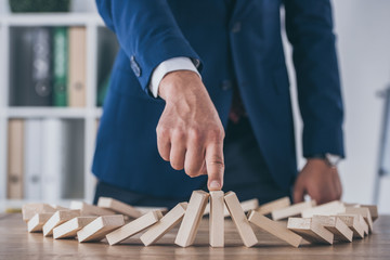 cropped view of risk manager stopping domino effect of falling wooden blocks