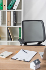 selective focus of office chair and rack with folders near desk with clipboard, calculator and house