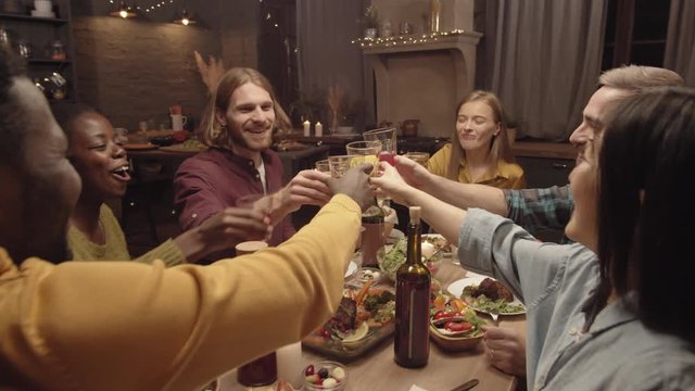 Handheld tracking shot of group of happy friends laughing and clanking glasses at dinner party