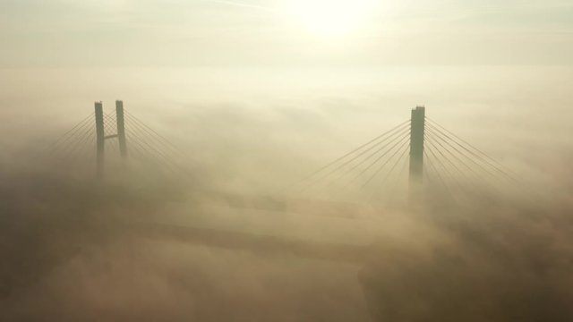 Aerial view of the fog passing through the Siekierkowski, Bridge. Warsaw. Aerial of the towers of the bridge with the movement of vehicles and a yacht passing along the river hung on a foggy morning.