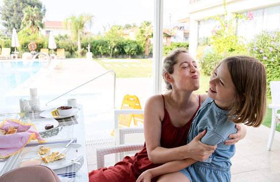 mother and daughter by the pool side having breakfast with mum trying to kiss