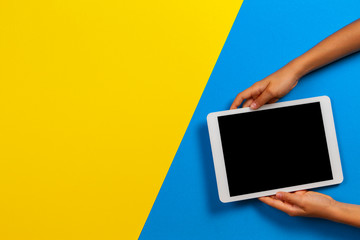 Kid hand with tablet computer on yellow and light blue background