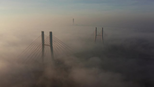 Aerial view of the landmark of the bridge in the fog in Warsaw. Drone flies above the clouds of fog and the Vistula river at sunrise. Spectacular Sunrise with low fog. bridge Siekierkowski, Warsaw.
