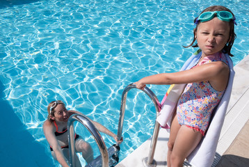 Mother and daughter playing at a swimming pool with daughter pulling faces