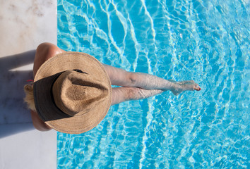 Woman sitting on the steps of a swimming pool with a hat on from overhead