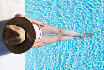 Woman sitting on the steps of a swimming pool with a hat on from overhead