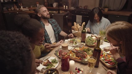 Handheld high angle shot of group of happy friends laughing and chatting at dinner party