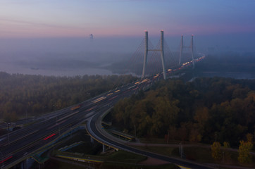 Aerial view of the fog passing through the Siekierkowski, Bridge. Warsaw. Aerial of the towers of the bridge with the movement of vehicles and a yacht passing along the river hung on a foggy morning.