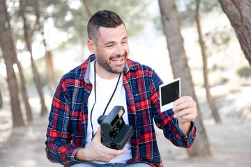 Hombre joven con camisa de cuadros obeservando una fotografia de una camara instantanea en el...