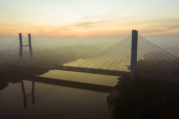 Aerial view of a bridge with cars in the fog. Warsaw. Poland. Drone shot at the traffic of a vehicle traveling in traffic jam on a bridge over a river. Drone shot into the fog at sunrise over a bridg