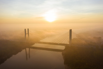 Aerial view of the fog passing through the Siekierkowski, Bridge. Warsaw. Aerial of the towers of the bridge with the movement of vehicles and a yacht passing along the river hung on a foggy morning.