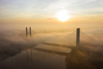 Obraz premium Aerial view of the Siekierkowski Bridge in beautiful fog. Warsaw, Poland. Drone shot at the traffic of vehicle traveling in traffic jam on a bridge over a river.